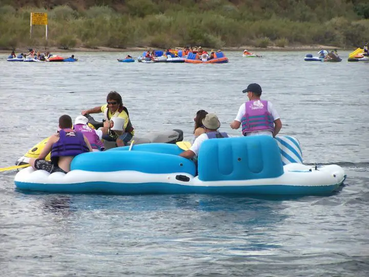 Large inflateble raft on the water with five people on it and a neighboring jetski with one person on it